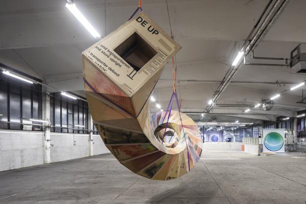 Eine spiralförmige Skulptur aus Kartons hängt in einer Lagerhalle.
