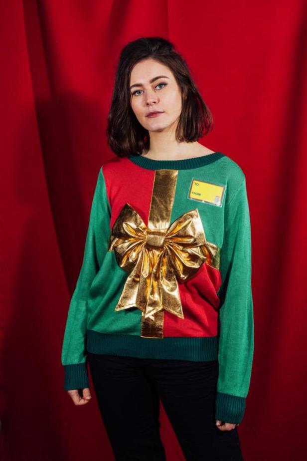 Eine Frau trägt einen Weihnachtspullover mit einer goldenen Schleife und einem Geschenkanhänger.