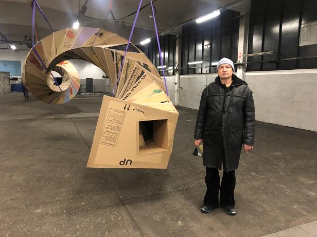 Ein Mann steht neben einer spiralförmigen Skulptur aus Kartons, die von der Decke hängt.