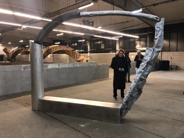 Eine Skulptur aus Metall und Stein steht in einer Lagerhalle.