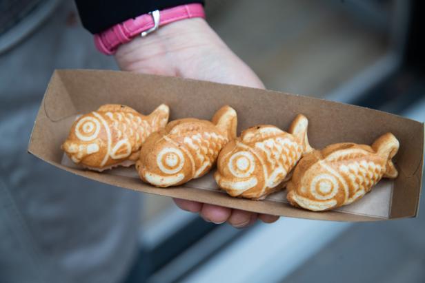 Eine Hand hält eine Pappschale mit vier Taiyaki-Fischwaffeln.