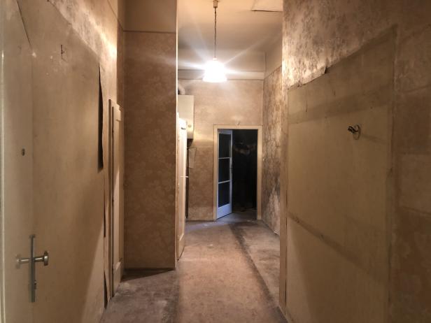 Ein Flur in einem renovierungsbedürftigen Haus mit abgenutzten Tapeten und einer Glühbirne an der Decke.