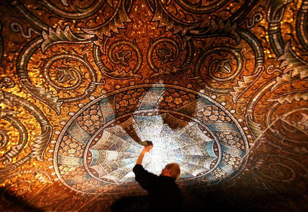 Ein Mann restauriert ein kunstvolles Mosaik an einer Decke.