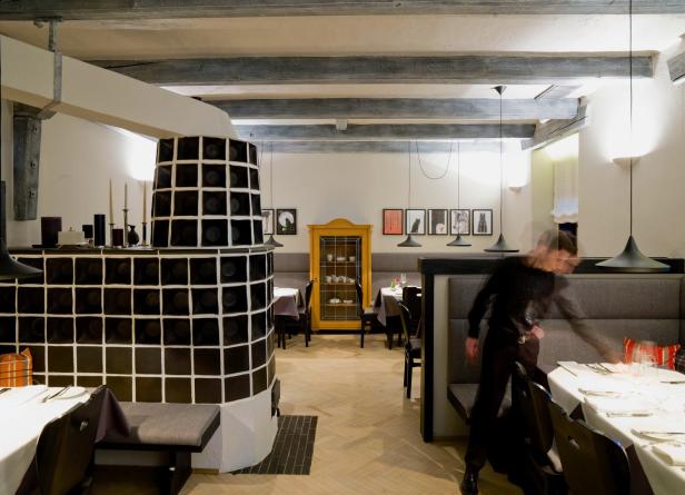 Ein Restaurant mit einem Kachelofen, Tischen und einem gelben Schrank im Hintergrund.