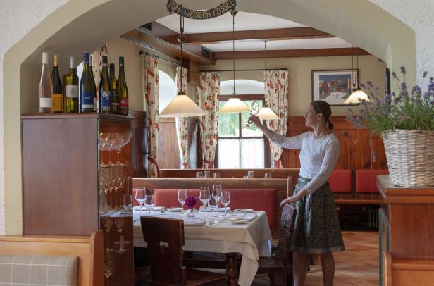 Eine Kellnerin im Dirndl überprüft ein Weinglas in einem traditionellen Restaurant.