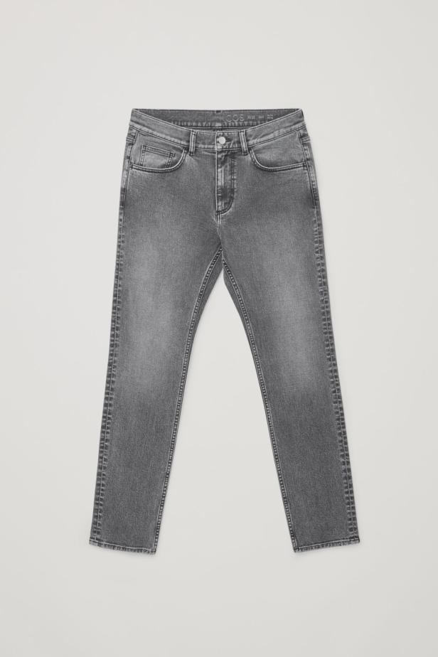 Eine graue Jeanshose liegt vor einem hellen Hintergrund.