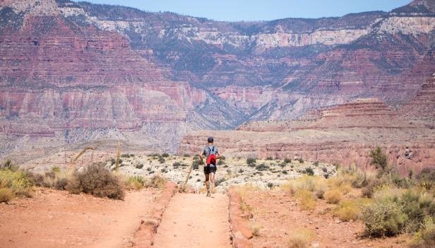 Ein Mann läuft mit einem roten Rucksack einen Pfad im Grand Canyon entlang.
