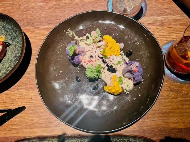 Ein Teller mit farbenfrohem Blumenkohl und einer hellen Sauce wird serviert.