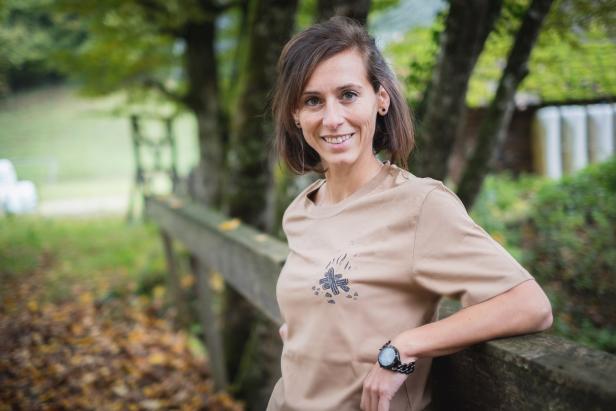 Eine lächelnde Frau lehnt an einem Holzzaun im Freien.