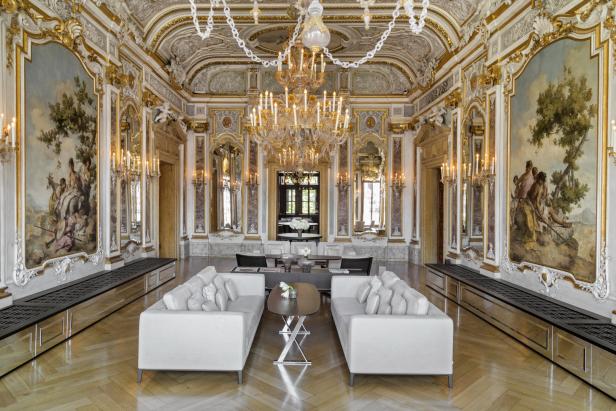 Ein prunkvoller Raum mit Gemälden, Spiegeln, Kristalllüstern und weißen Sofas.