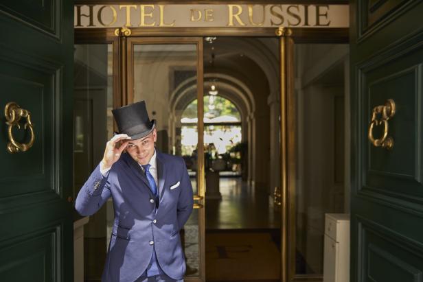 Ein Mann mit Zylinder und Anzug begrüßt vor dem „Hotel de Russie“.