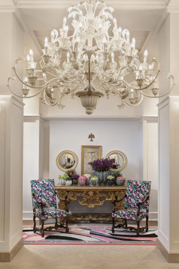 Ein eleganter Eingangsbereich mit einem verzierten Kronleuchter und einem goldenen Konsoltisch mit Blumenarrangements.