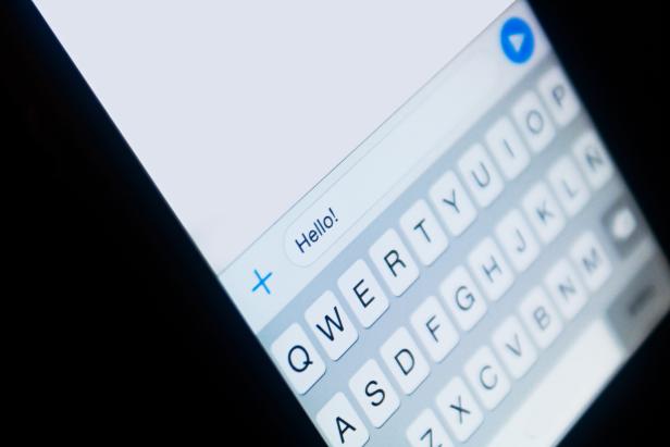 Nahaufnahme eines Smartphone-Bildschirms mit der Nachricht „Hello!“ und der Tastatur.