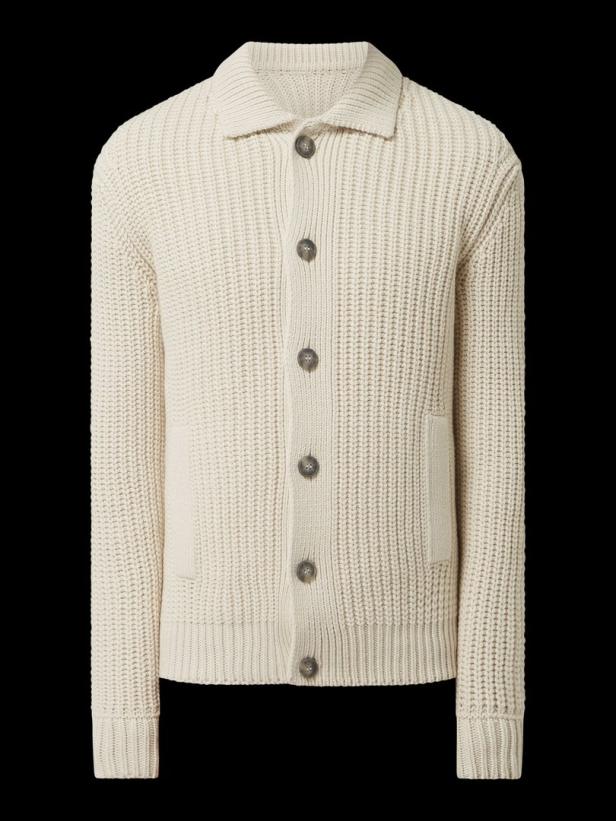 Eine cremefarbene Strickjacke mit Knöpfen und Kragen vor schwarzem Hintergrund.