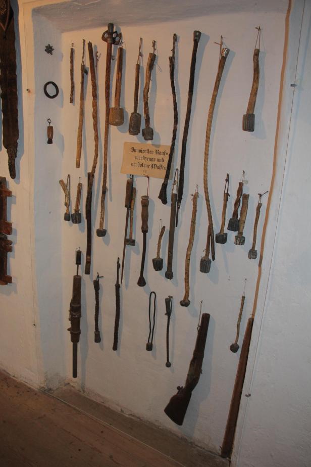 Eine Sammlung historischer Knüppel, Schlagstöcke und einer alten Flinte an einer Wand.