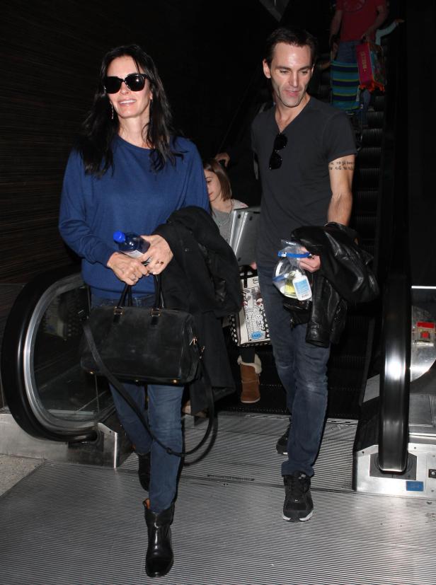 Courteney Cox und ein Mann fahren auf einer Rolltreppe nach unten.