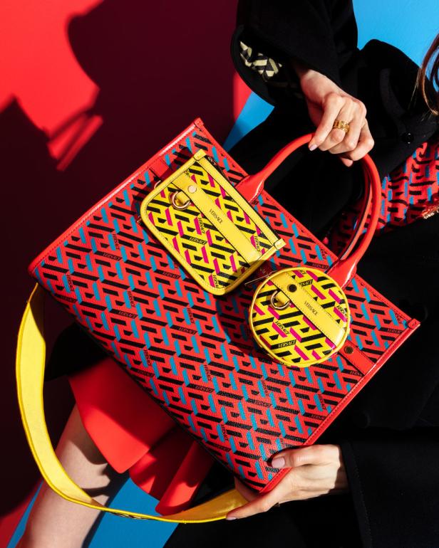 Eine Frau hält eine Versace-Tasche mit einem auffälligen geometrischen Muster in Rot, Gelb und Blau.