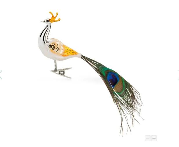 Ein dekorativer, weißer Pfau mit goldener Krone und langer, grüner Feder auf einem Clip.