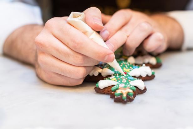Eine Person verziert Lebkuchen in Form von Weihnachtsbäumen mit Zuckerguss.