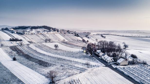 Eine verschneite Landschaft mit Weinbergen und einem kleinen Dorf.