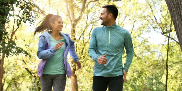 Ein Mann und eine Frau joggen lächelnd durch einen sonnigen Park.