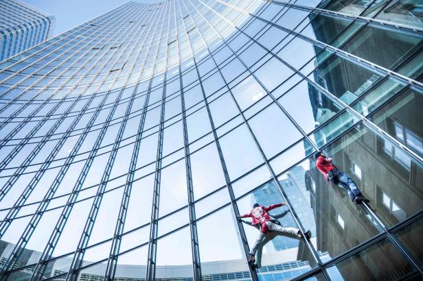 Zwei Fensterputzer arbeiten an der Fassade eines hohen Bürogebäudes.