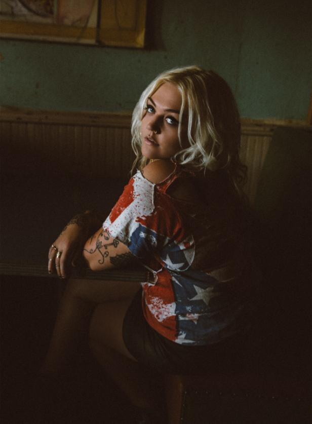 Elle King Eine junge Frau mit blonden Haaren und Tätowierungen blickt über ihre Schulter.