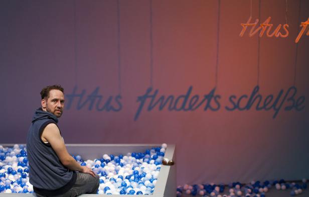 Ein Mann sitzt in einem Bällebad vor einer Wand mit der Aufschrift „Titus findet's scheiße“.