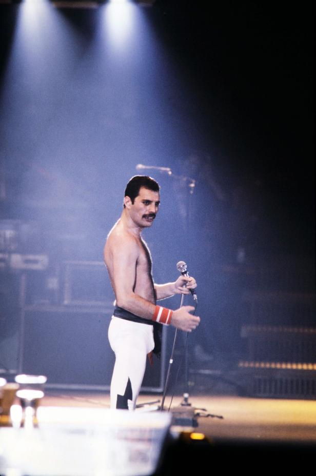 Freddie Mercury von Queen steht mit einem Mikrofon auf der Bühne.