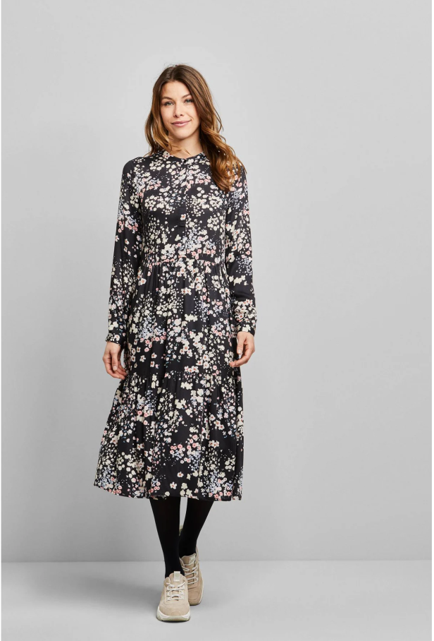 Eine Frau trägt ein schwarzes, geblümtes Kleid mit langen Ärmeln und schwarzen Strumpfhosen.