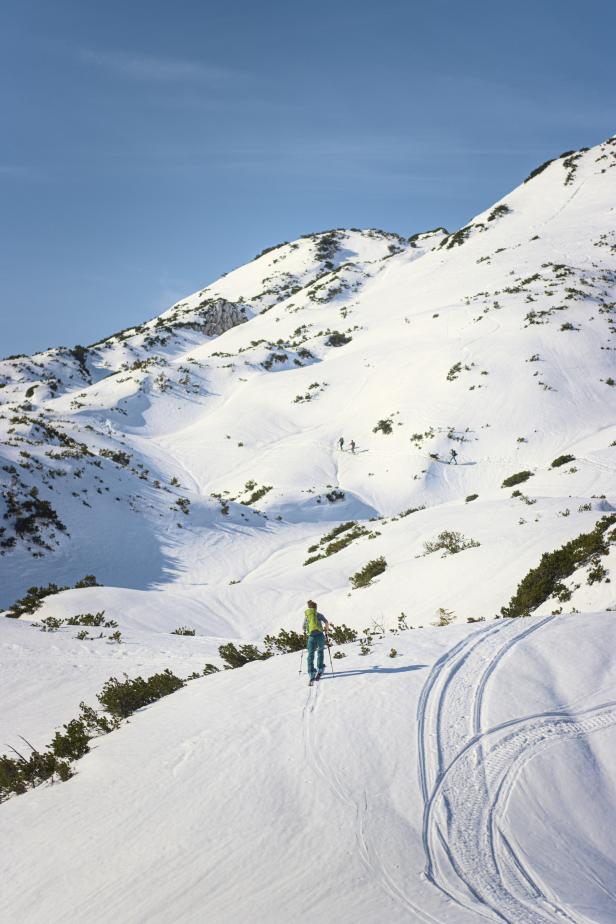 Eine Frau geht mit Skiern einen verschneiten Hang hinauf.