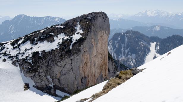 Ein Bergmassiv mit einem Gipfelkreuz und Schneeflächen im Gebirge.