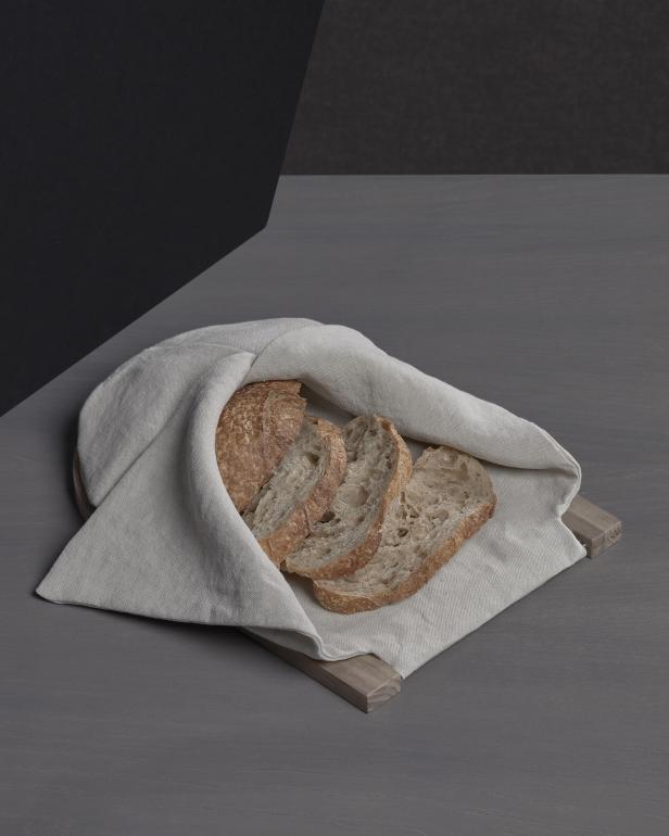 Ein Laib Brot und einige Scheiben Brot liegen in einem Leinentuch auf einem Holzbrett.
