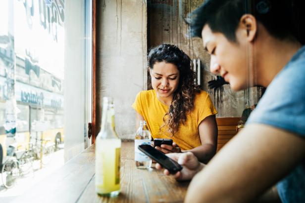 Eine Frau und ein Mann sitzen in einem Café und schauen auf ihre Smartphones.