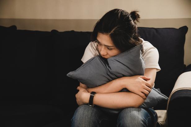 Eine junge Frau sitzt auf einem Sofa und umarmt ein Kissen.