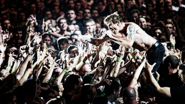 Ein Sänger mit Tätowierungen singt auf den Händen einer Menschenmenge.