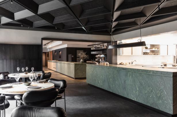 Innenansicht eines eleganten Restaurants mit Tischen und einer Bar aus grünem Marmor.