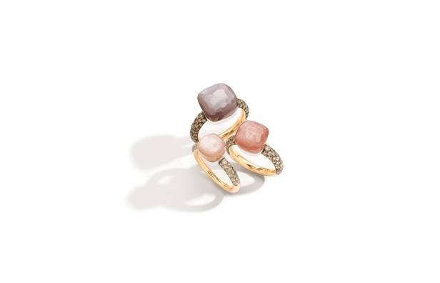 Drei goldene Ringe mit quadratischen Edelsteinen in Rosa- und Grautönen liegen auf einem weißen Hintergrund.