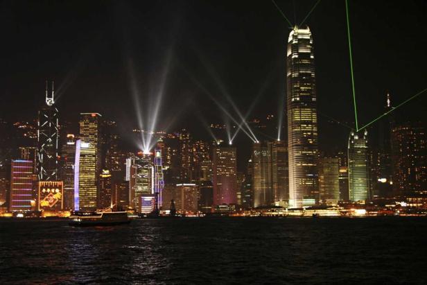 Die Skyline von Hongkong erstrahlt nachts mit Lichtern und einem Boot auf dem Wasser.