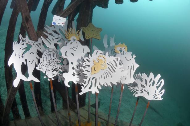 Unterwasser-Kunstinstallation mit ausgeschnittenen Meerestieren und Korallen an Metallstäben.
