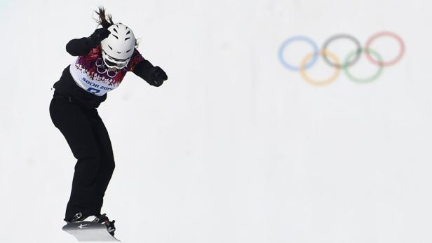 Eine Snowboarderin springt vor dem Hintergrund der Olympischen Ringe.