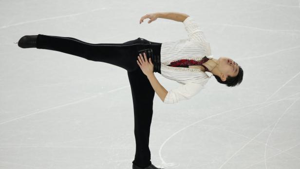 Ein Eiskunstläufer in einem weißen Hemd und schwarzer Hose führt eine Drehung auf dem Eis aus.