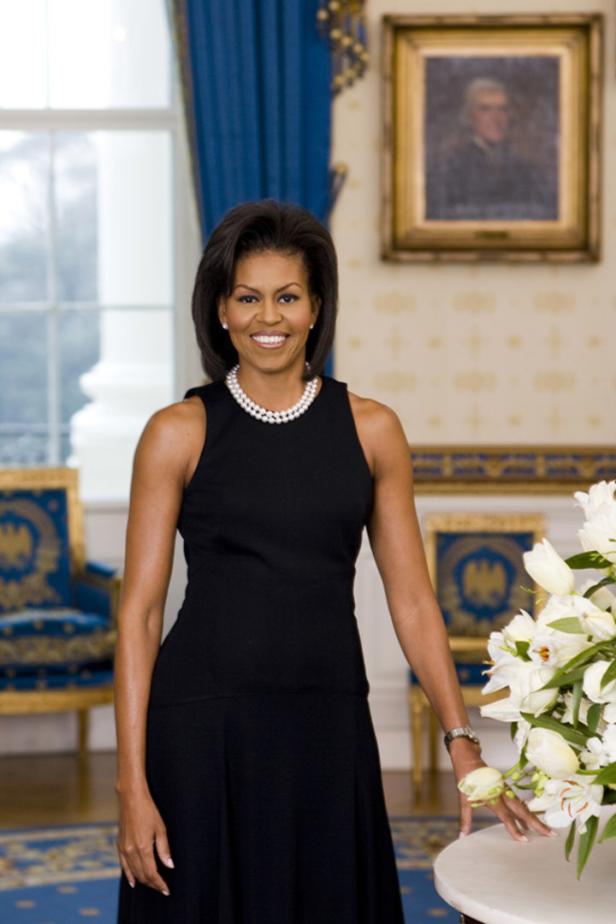 Michelle Obama in einem schwarzen Kleid und einer Perlenkette lächelt.