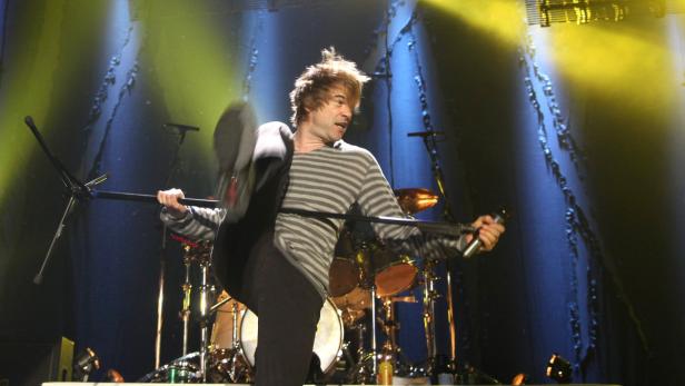 Ein Sänger tritt auf der Bühne gegen ein Mikrofonstativ.