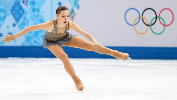 Eine Eiskunstläuferin während einer Kür vor dem Hintergrund der Olympischen Ringe.