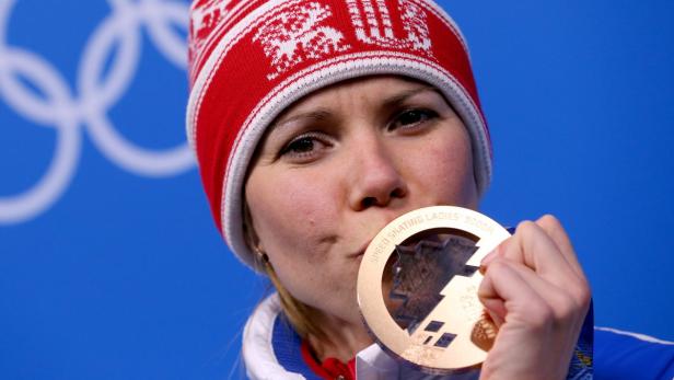 Eine Frau mit roter Mütze küsst ihre Goldmedaille vor dem Hintergrund der olympischen Ringe.