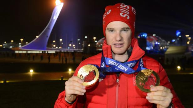 Ein Sportler mit zwei Goldmedaillen vor dem olympischen Feuer in Sotschi 2014.