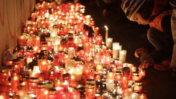 Ein Kind kniet vor einer Vielzahl von brennenden Kerzen.