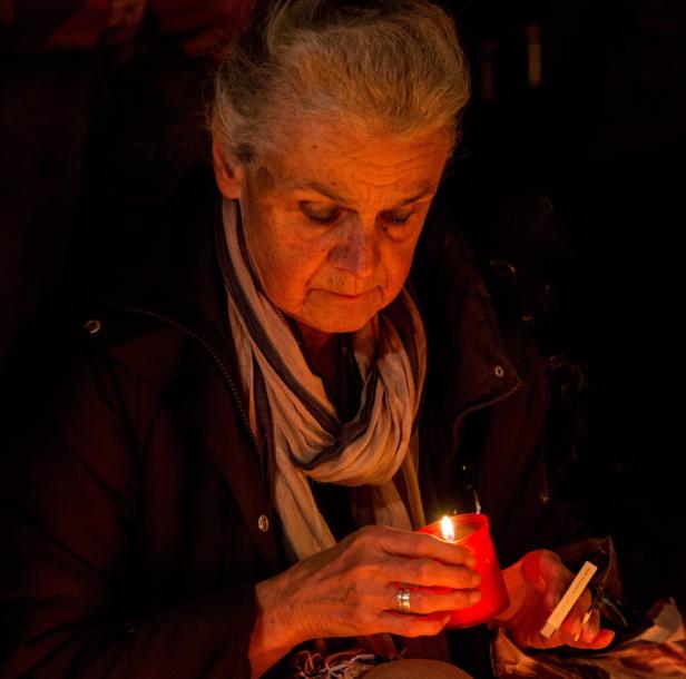 Eine ältere Frau zündet eine Kerze in einem roten Glas an.