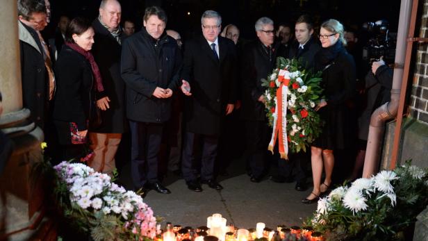 Eine Gruppe von Menschen steht vor einem Denkmal mit Blumen und Kerzen.
